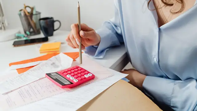Persona haciendo cuentas con una calculadora y facturas sobre el escritorio